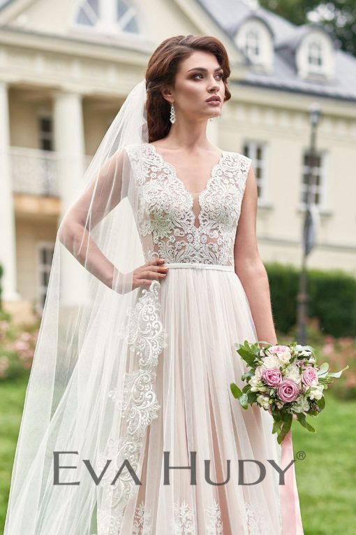 Subtelna suknia ślubna. Jej górna część, wykonana z wyrazistej koronki, jest dość zabudowana, co nadaje całości elegancji. Osadzona na grubych ramiączkach.
